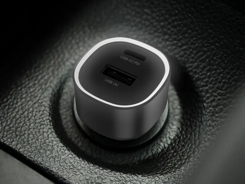 Czarna ładowarka samochodowa z dwoma portami: USB-C oznaczonym jako \'USB (C) PD\' i USB-A oznaczonym jako \'USB (A)\', umieszczona w gnieździe samochodowym.