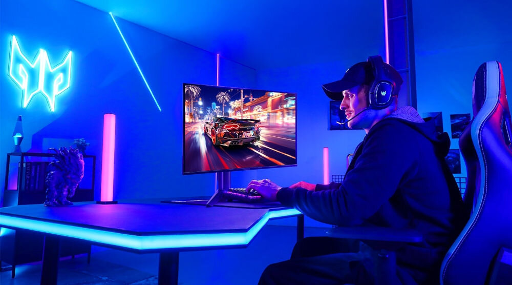 Monitor ACER Predator X27UZ1BMIIPRX 26.5 cala 2560x1440px OLED 280Hz 0.03 [GTG] prezentacja monitora podczas użytkowania mężczyzna siedzący przy biurku w oświetlonym na niebiesko pokoju na ekranie gra samochodowa
