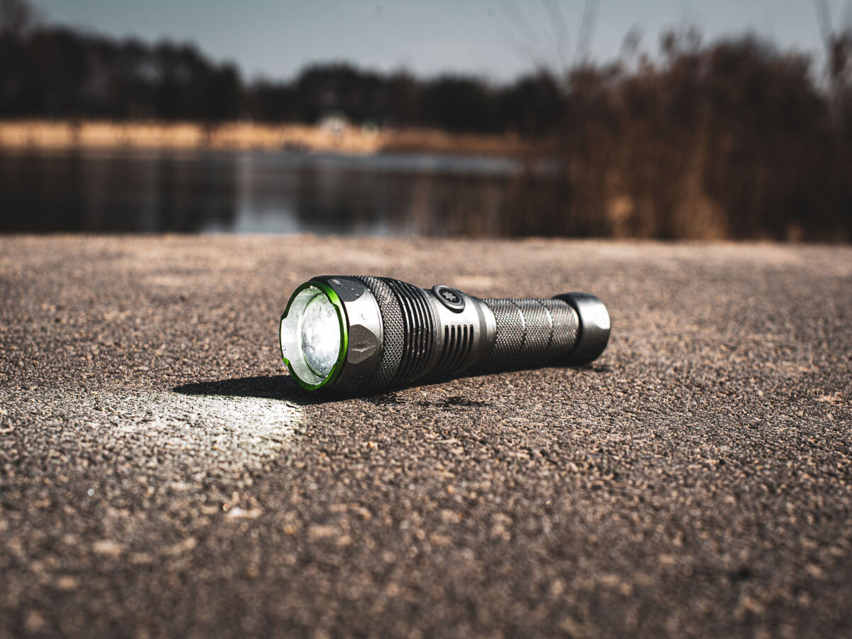Latarka taktyczna VAYOX VA0364, 3000 lumenów w Twojej dłoni, Latarka leży włączona na asfalcie, w tle jezioro