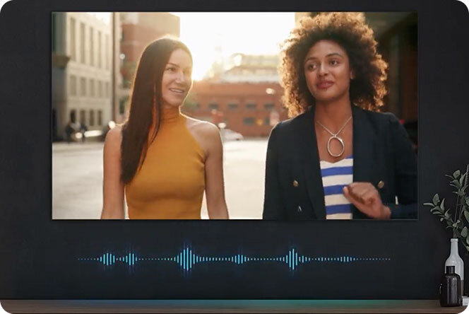 Grafika przedstawiająca telewizor z widocznymi dwoma kobietami na ekranie. Grafika podkreśla działania fukcji adapracji dźwięku PRO w telewizorze Samsung The Frame (2025)