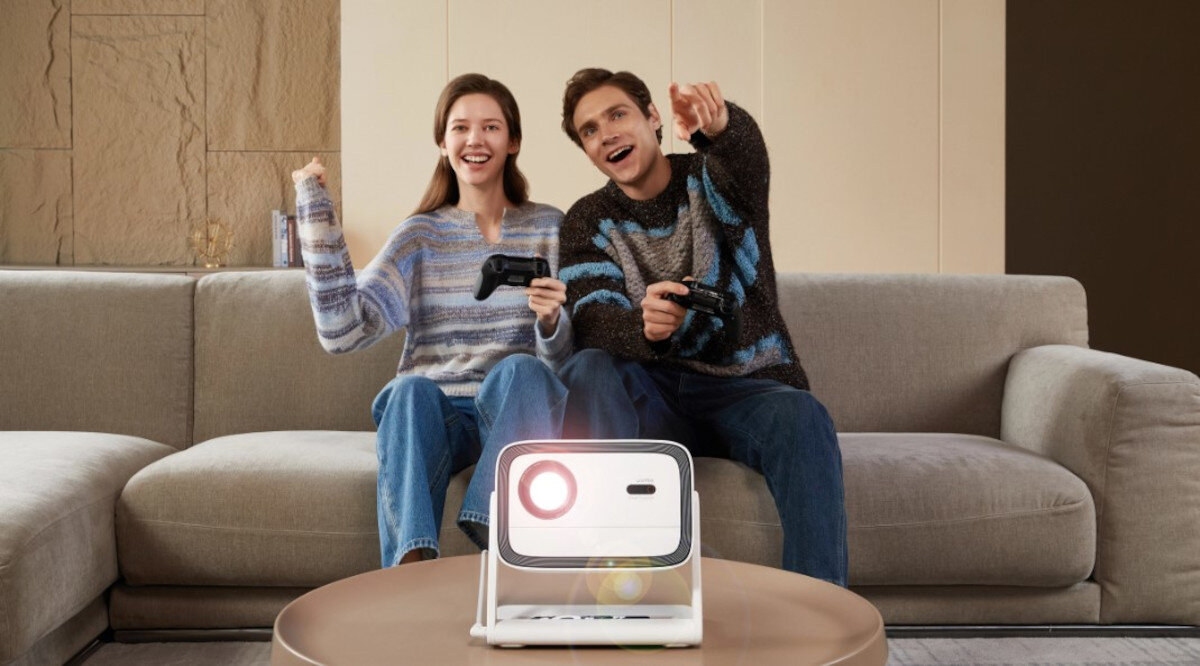 WANBO Vali 1 projektor ekran 102-330 cm elastyczna projekcja, osoby siedzące na kanapie z kontrolerami w ręku, projektor stojący na stoliku wyświetlający obraz