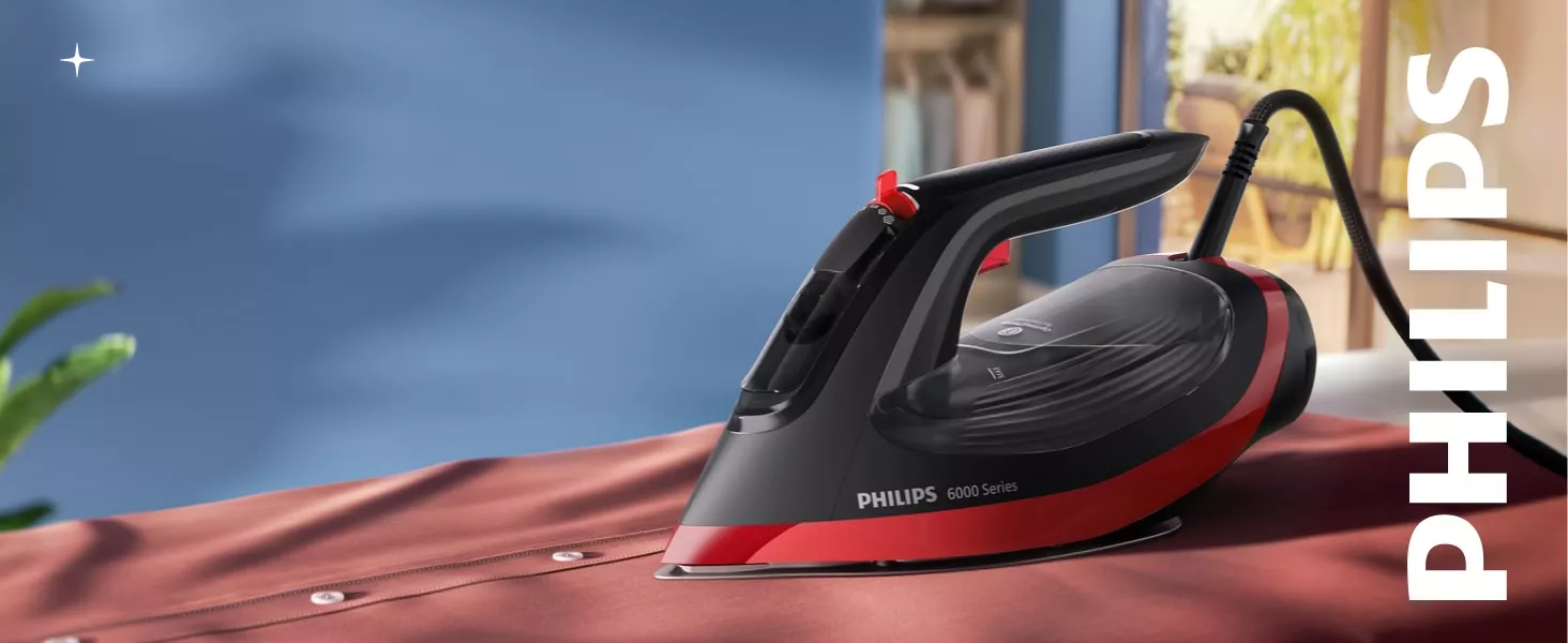 Żelazko z serii PHILIPS 6000 Series znajduje się na tkaninie, z widocznym logo PHILIPS na obudowie. W tle widać rozmyty fragment wnętrza z rośliną.