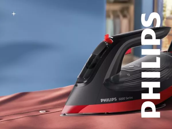 Żelazko z napisem \'PHILIPS 6000 Series\' stoi na brązowej tkaninie. W tle widoczna jest rozmyta przestrzeń w odcieniach niebieskiego.