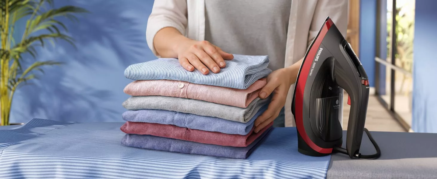 Osoba układa stos wyprasowanych koszul na desce do prasowania obok żelazka z napisem \'PHILIPS 6000 Series\'.