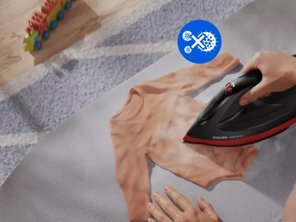 Osoba prasuje pomarańczową koszulkę żelazkiem z napisem \'PHILIPS 6000 Series\'. W tle widoczne są kolorowe zabawki i niebieska ikona z symbolem zębatki i wirusa.
