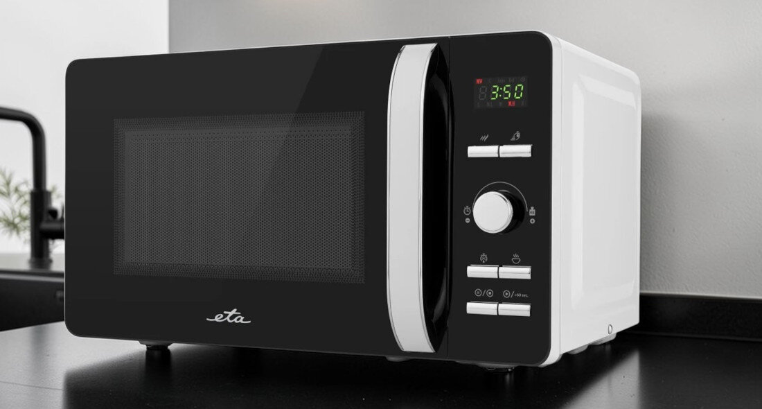 Kuchenka mikrofalowa ETA Gavento ETA120990000 Zdjęcie ukazuje tę samą kuchenkę mikrofalową ustawioną na czarnym blacie kuchennym, na tle jasnej ściany i fragmentu armatury. Czarno‑biały korpus urządzenia kontrastuje z otoczeniem, a front z wyświetlaczem i pokrętłami jest dobrze wyeksponowany równomierne grzanie kontrola czasu wyświetlacz cyfrowy timer 60 minut oświetlenie wnętrza