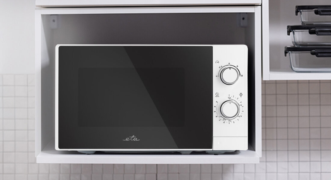 Kuchenka mikrofalowa ETA Marvello ETA421090000 Zdjęcie ukazuje kuchenkę mikrofalową ETA umieszczoną we wnęce meblowej, co podkreśla jej kompaktowe wymiary i możliwość zabudowy. Widoczny jest czytelny panel sterowania z dwoma pokrętłami po prawej stronie biała kompaktowa szybkie podgrzewanie oszczędność czasu 700W rozmrażanie wygoda