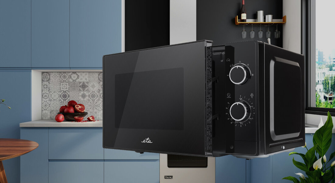 Czarna kuchenka mikrofalowa z logo \'eta\' na drzwiczkach, umieszczona w nowoczesnej kuchni z niebieskimi szafkami. Na panelu bocznym znajdują się dwa pokrętła do regulacji ustawień.