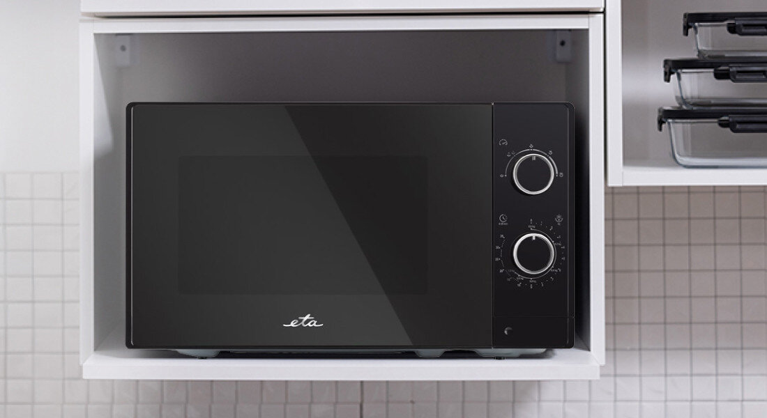 Czarna kuchenka mikrofalowa z dwoma pokrętłami na panelu przednim, umieszczona w białej wnęce kuchennej. Na drzwiczkach widoczne jest logo \'eta\'.