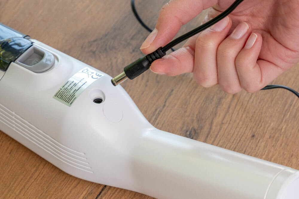 Odkurzacz ręczny GÖTZE & JENSEN HV800 Zbliżenie na rękę wkładającą końcówkę ładowarki (czarny wtyk DC) do gniazda ładowania umieszczonego w korpusie ręcznego odkurzacza Gotze & Jensen HV800