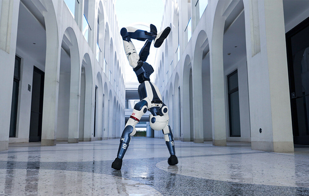 Robot humanoidalny stoi na rękach w korytarzu z jasną podłogą i powtarzającymi się białymi łukami