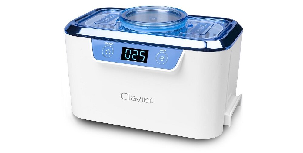Biała myjka ultradźwiękowa z niebieskim wyświetlaczem pokazującym \'025\' oraz przyciskami oznaczonymi symbolami włączania i czasu. Na obudowie widoczne jest logo \'Clavier\'.