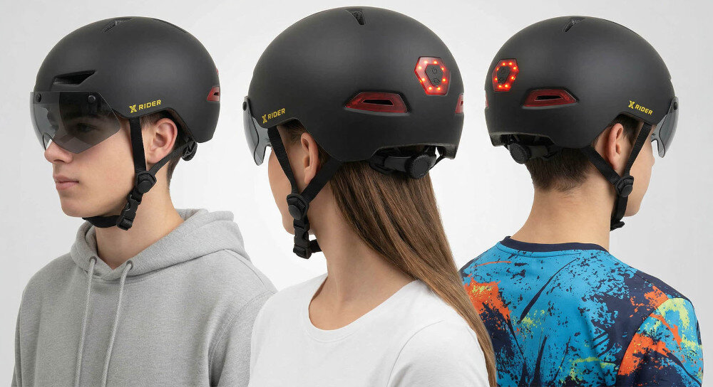 Trzy osoby noszą czarne kaski XRIDER z przyciemnianą szybą i wbudowanymi lampkami LED z tyłu. Na kaskach widoczne jest logo \'X RIDER\'.