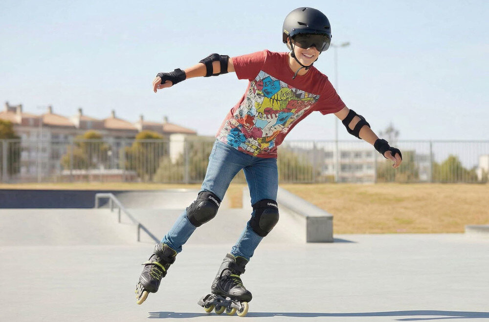 Osoba na rolkach w skateparku nosi czarny kask i ochraniacze. W tle widać budynki i niebo.