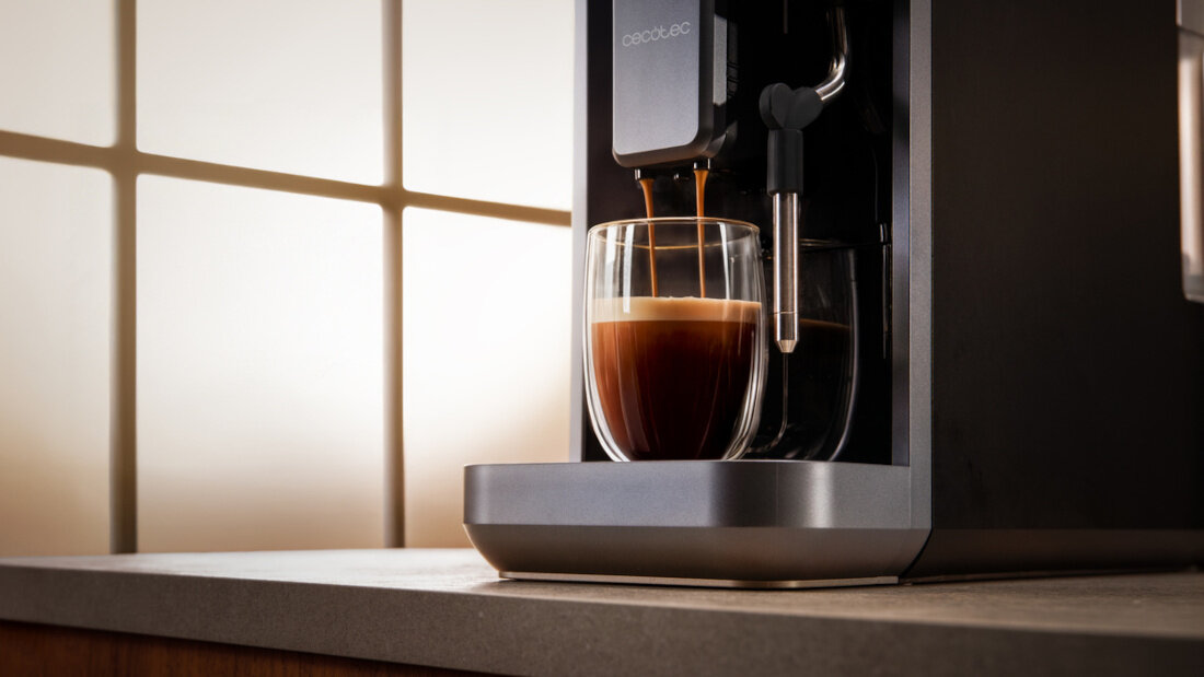 Ekspres do kawy nalewa kawę do szklanki, na której powierzchni widać warstwę pianki. Na urządzeniu widoczne jest logo \'cecotec\'.