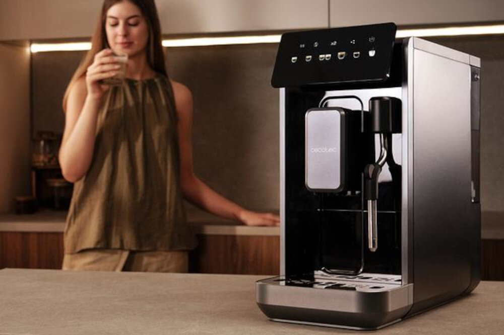 Na blacie kuchennym stoi ekspres do kawy z panelem dotykowym i logo \'CECOTEC\'. W tle widoczna jest osoba trzymająca filiżankę.