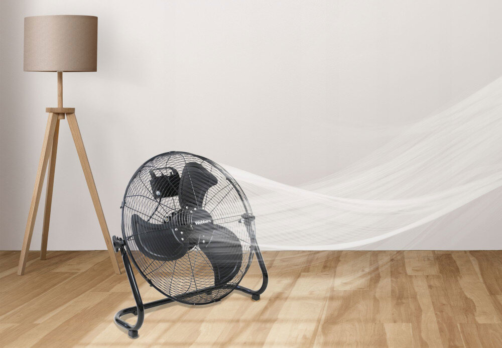 Na drewnianej podłodze stoi czarny wentylator z widocznym logo \'WEBBER\' na osłonie. Obok znajduje się lampa stojąca z beżowym abażurem, a z wentylatora wydobywa się wizualizacja przepływu powietrza.