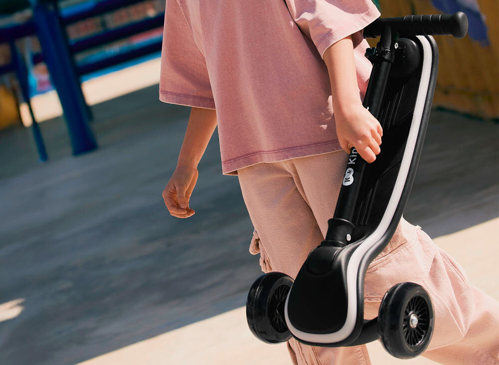 Hulajnoga dla dzieci KINDERKRAFT Raket Beżowy skatepark dziecko niesie w dłoni hulajnogę aktywność zabawa środek transportu