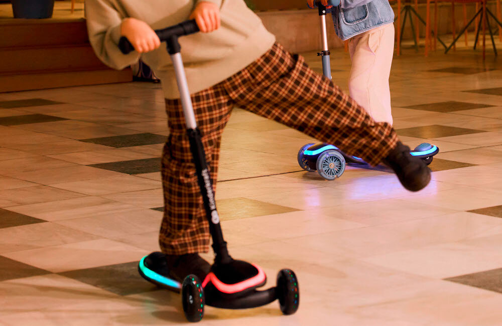 Hulajnoga dla dzieci KINDERKRAFT Raket Beżowy miasto dziecko jedzie na hulajnodze na drugim planie drugie dziecko na hulajnodze w tle krzesładla dzieci od 2. roku życia wspiera rozwój koordynacji i równowagi stabilna konstrukcja z dwoma przednimi i szerokim tylnym kołem uczy aktywności i samodzielności