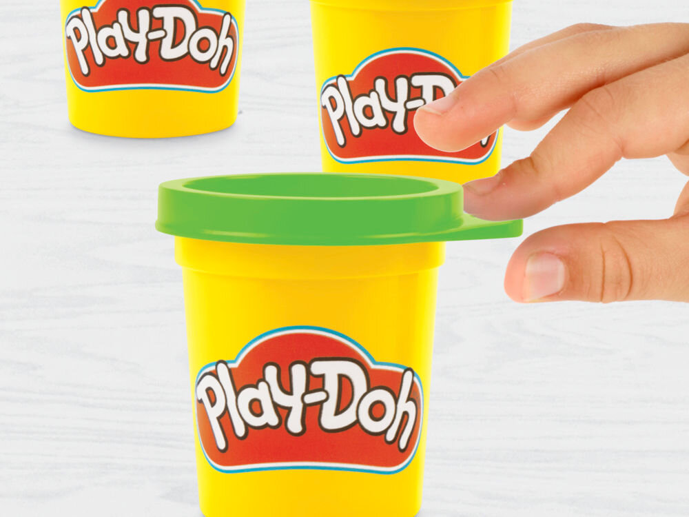 Ciastolina PLAY-DOH Disney Junior Mickey Mouse Przenośny garaż Zbliżenie na dłoń dziecka otwierającą żółty pojemnik ciastoliny Play-Doh z zieloną pokrywką. W tle widoczne dwa kolejne kubeczki z masą plastyczną ustawione na białym blacie.