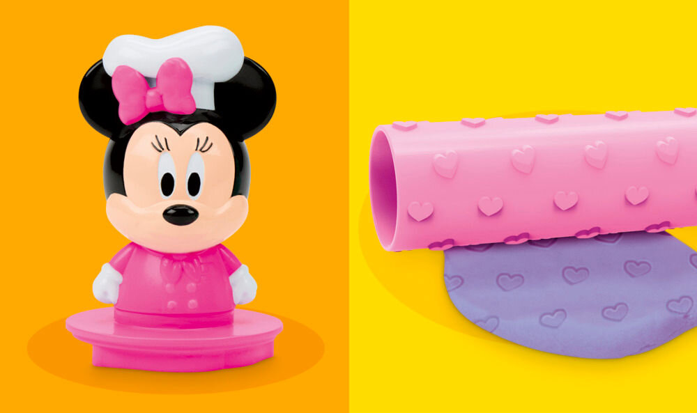 Ciastolina PLAY-DOH Disney Junior Mickey Mouse Przenośna cukiernia G31085X0 Zbliżenie na figurkę Myszki Minnie w stroju kucharki oraz różowy wałek do ciastoliny z wypukłym wzorem w serca, pozostawiający odciski na fioletowej masie plastycznej.