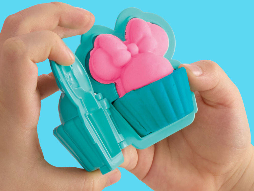 Ciastolina PLAY-DOH Disney Junior Mickey Mouse Przenośna cukiernia G31085X0 Dłonie dziecka używające dwuczęściowej, turkusowej foremki Play-Doh do formowania babeczki z różowej ciastoliny z motywem kokardy Myszki Minnie.