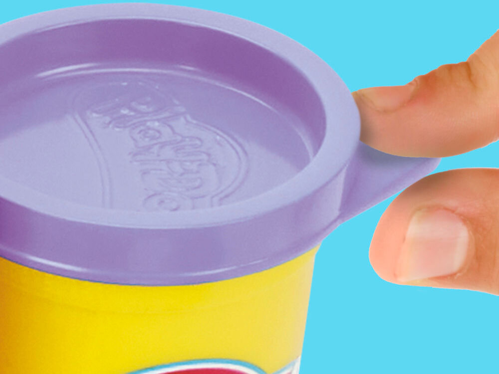 Ciastolina PLAY-DOH Disney Junior Mickey Mouse Przenośna cukiernia G31085X0 Zbliżenie na palce dziecka otwierające żółty pojemnik z ciastoliną Play-Doh z fioletową pokrywką, na której widoczne jest wytłoczone logo marki.