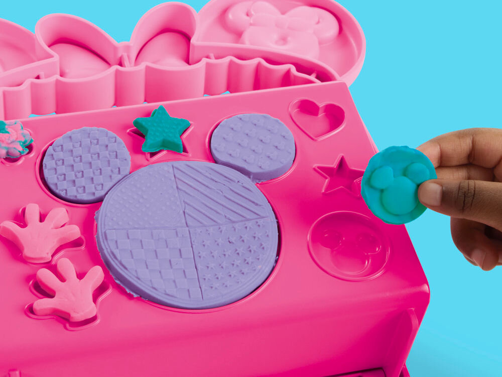 Ciastolina PLAY-DOH Disney Junior Mickey Mouse Przenośna cukiernia G31085X0 Prezentacja spodu różowej walizeczki Play-Doh, która służy jako platforma z foremkami. Widoczne odciśnięte kształty gwiazdek, serc oraz głowy Myszki Miki w różnych kolorach masy.