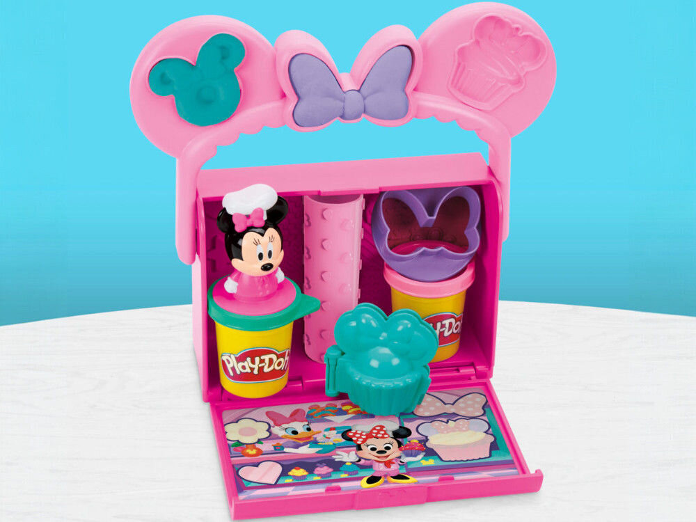 Ciastolina PLAY-DOH Disney Junior Mickey Mouse Przenośna cukiernia G31085X0 Wnętrze otwartej walizeczki Play-Doh z uporządkowanymi akcesoriami: dwiema tubami ciastoliny, figurką Minnie, wałkiem i foremkami. Na klapie widoczna kolorowa ilustracja ze świata Disneya.
