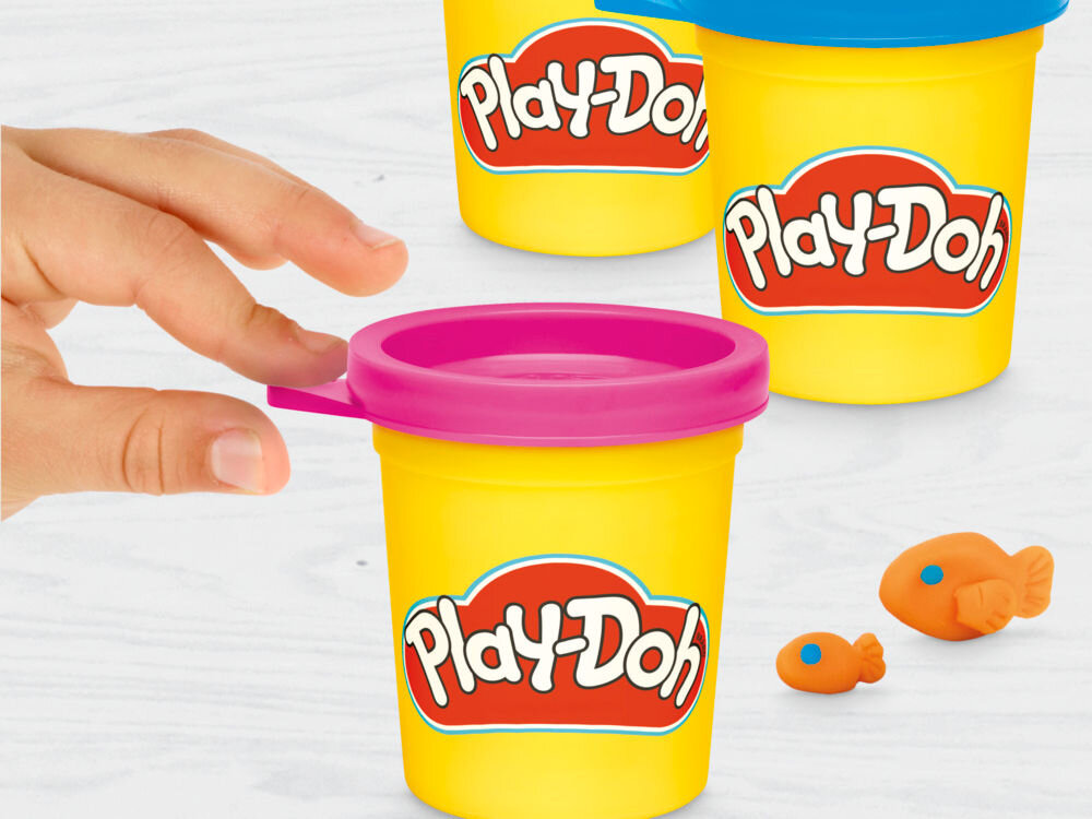 Ciastolina PLAY-DOH Disney Junior zestaw pieczątek G31105L0 Zbliżenie na dłoń dziecka zdejmującą zieloną pokrywkę z żółtego pojemnika ciastoliny Play-Doh. W tle widoczne kolejne kubeczki z masą plastyczną przygotowane do zabawy.
