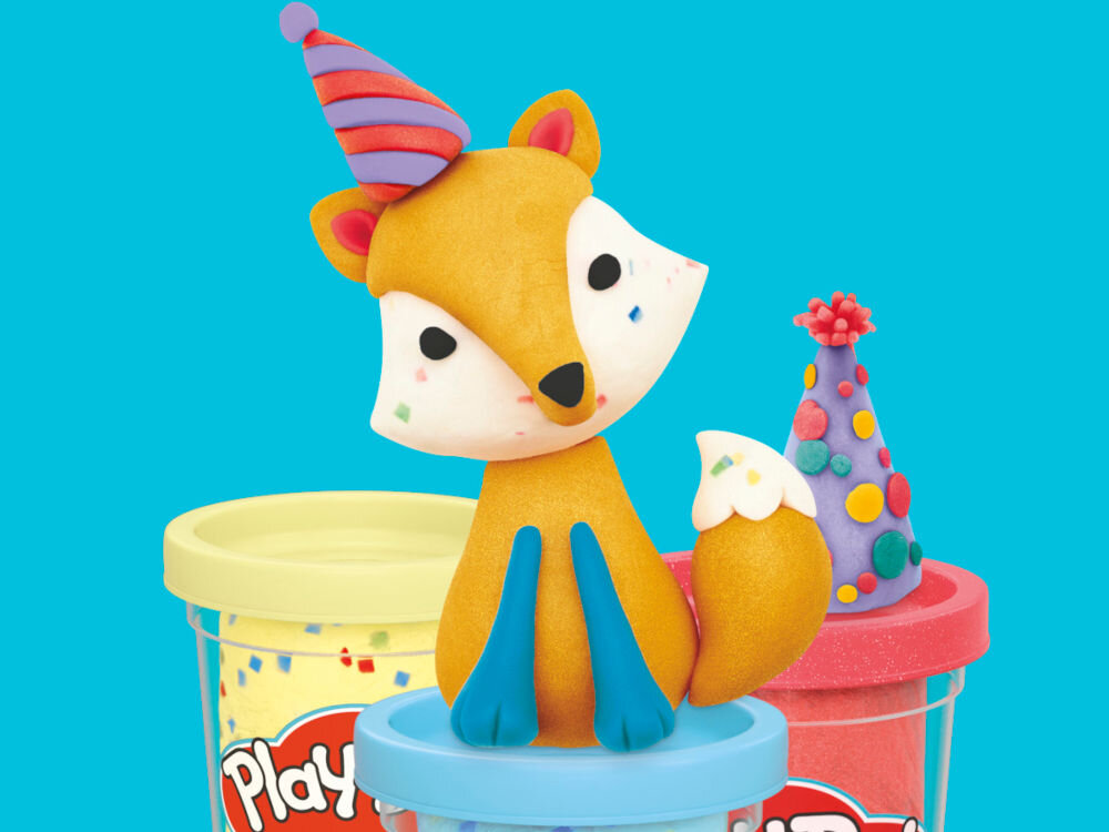 Ciastolina PLAY-DOH Twórz i świętuj zestaw 20 tub G24675L0 Zbliżenie na figurkę Myszki Minnie w stroju kucharki oraz różowy wałek Play-Doh z wypukłym wzorem w serca, który pozostawia dekoracyjne odciski na fioletowej masie plastycznej rozwałkowanej na białym blacie.