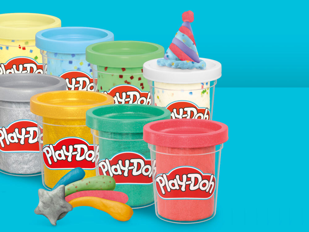 Ciastolina PLAY-DOH Twórz i świętuj zestaw 20 tub G24675L0 Zbliżenie na palce dziecka zdejmujące fioletową pokrywkę z żółtego pojemnika ciastoliny Play-Doh. Na pokrywce widoczne jest wytłoczone logo marki, a produkt jest zaprojektowany tak, by był łatwy do otwarcia dla małych rączek.
