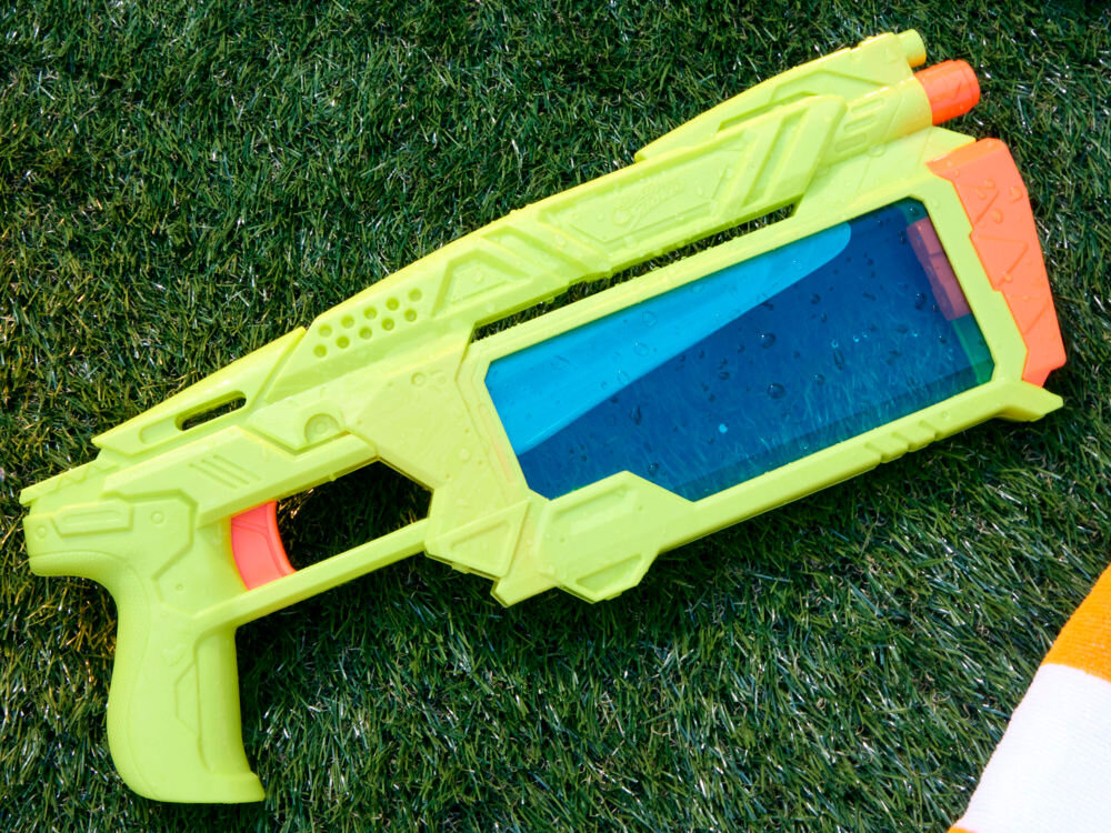 Wyrzutnia NERF Super Soaker Dunk-Fill+ G21465L0 Limonkowo-pomarańczowa wyrzutnia wodna Nerf Super Soaker z przezroczystym niebieskim zbiornikiem, leżąca na trawie.