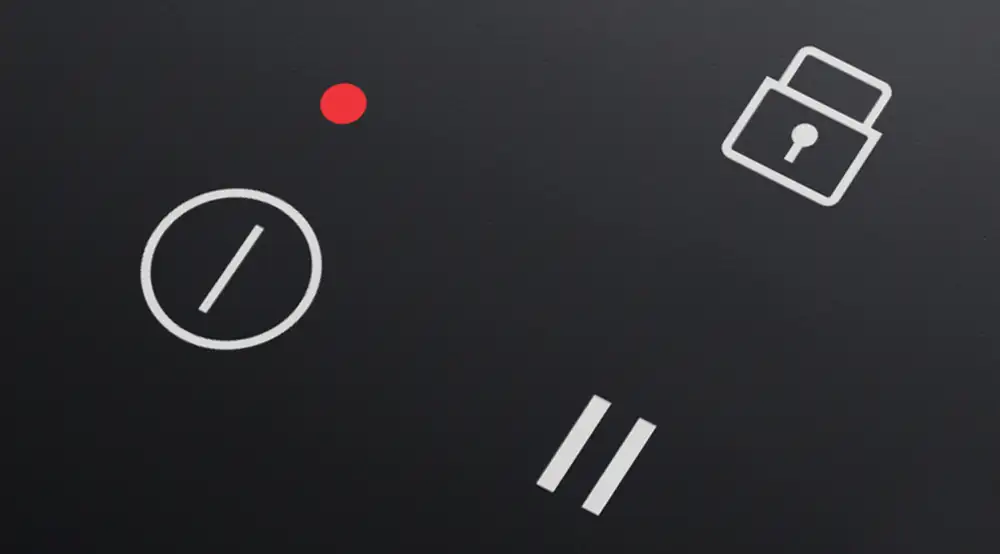 Obraz przedstawia panel sterowania płyty indukcyjnej z ikonami: czerwony punkt, symbol włącznika, symbol kłódki oraz symbol pauzy. Tło jest czarne, a ikony są białe.