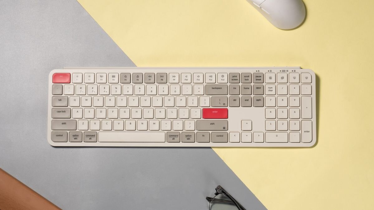 Keychron B6 Pro - Klawiatura ułożona na dwukolorowej podkładce na biurku, obok myszy komputerowej oraz okularów.
