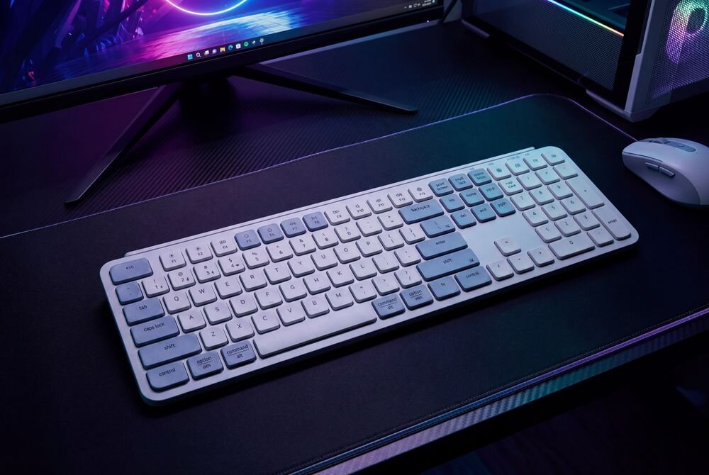 Keychron B6 Pro Keychron B6 Pro akumulator o pojemności 800 mAh 1200 godzin pracy na jednym ładowaniu 5 godzin dziennie 8 miesięcy działania pracę podczas ładowania przez USB-C - Klawiatura umieszczona na stanowisku komputerowym z widocznym fragmentem monitora oraz podświetleniem gamingowym.