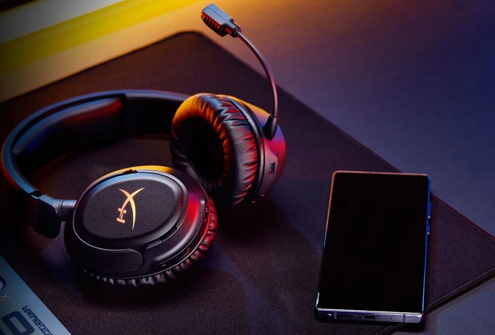 Słuchawki HYPERX Cloud Flight 2 łączność 2,4 GHz Bluetooth Instant Pair bezprzewodowe, słuchawki leżące obok smartfona na podkładce na biurko