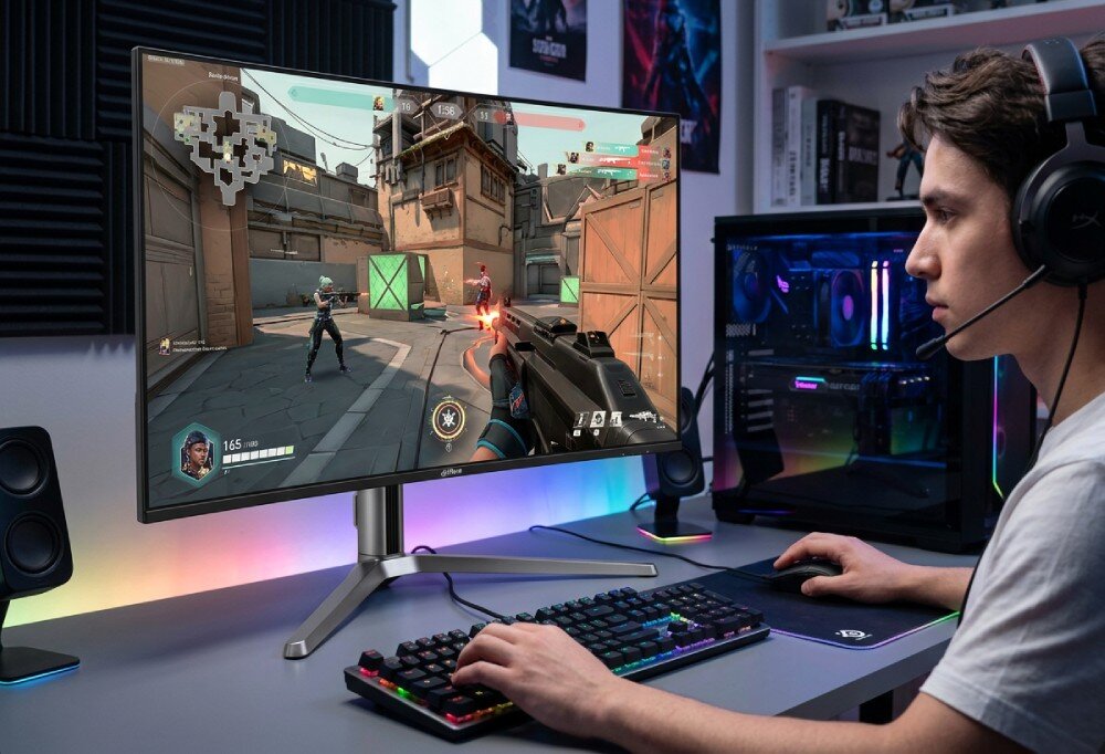 Monitor DAHUA LM32-GO43A Mężczyzna w słuchawkach gra w grę akcji na zakrzywionym monitorze ustawionym na biurku obok komputera stacjonarnego