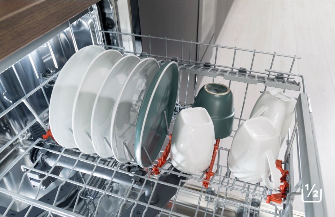 ZMYWARKA HISENSE HV543D10 Wnętrze zmywarki z częściowo wypełnionym górnym koszem, w którym stoją talerze i kubki, a w dolnym rogu widnieje ikona „1/2”, podkreślająca funkcję mycia przy połowie załadunku