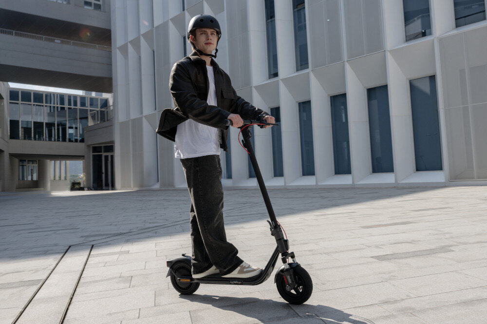 Hulajnoga elektryczna SEGWAY F2 Pro D II 65km 900W 10 cali Czarny miasto osoba jedzie na hulajnodze po drodze w tle budynek środek codziennego transportu styl stabilność bezpieczeństwo