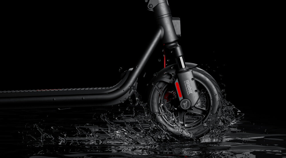 Hulajnoga elektryczna SEGWAY F2 Pro D II 65km 900W 10 cali Czarny ciemne tło zbliżenie na przednie koło koło umoczone w kałuży rozchlapana woda klasa wodoodporności IPX5 odporność na silne strumienie wody zapewnia stabilne działanie solidna konstrukcja odporne materiały ergonomiczny kształt intuicyjna obsługa komfort bezpieczeństwo