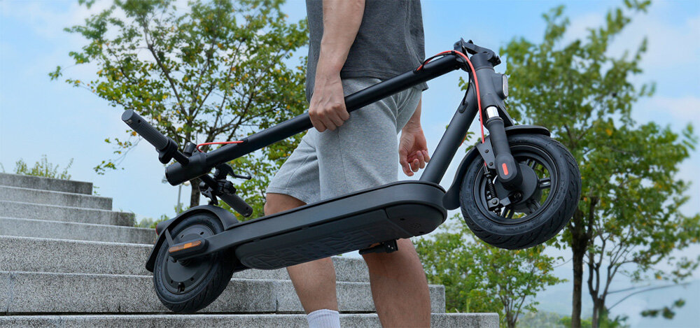 Hulajnoga elektryczna XIAOMI Scooter Elite 45km 400W 10 cali Czarny osoba niesie złożoną hulajnogę w ręku do jazdy po mieście dynamiczne ekscytujące podróżowanie szereg udogodnień praktyczne rozwiązania styl moc wygoda