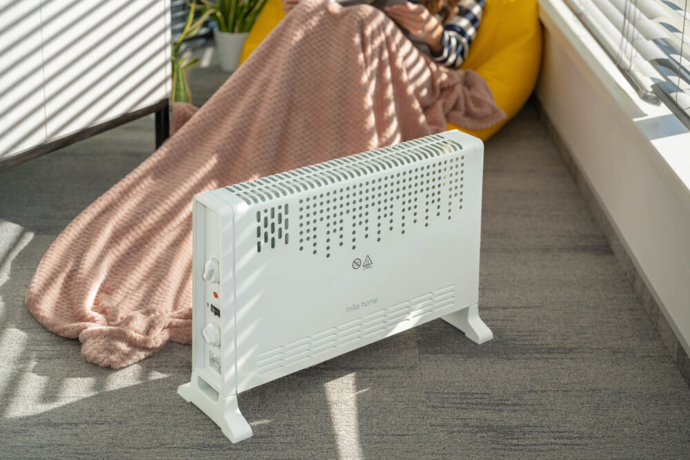 Grzejnik konwektorowy MILLA HOME MCH104 system zabezpieczający grzejnik stojący w tle fotel nakryty kocem