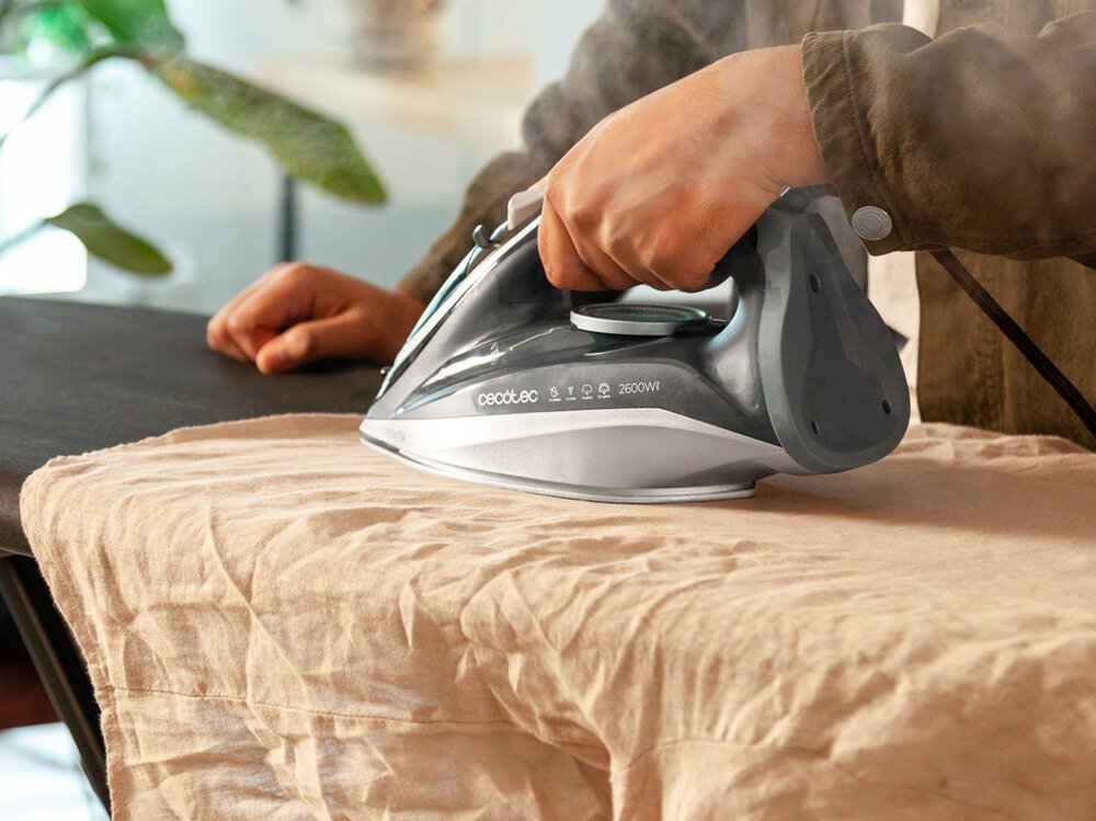 Osoba prasuje tkaninę za pomocą żelazka z widocznym napisem \'cecotec 2600W\'. W tle widać roślinę doniczkową.