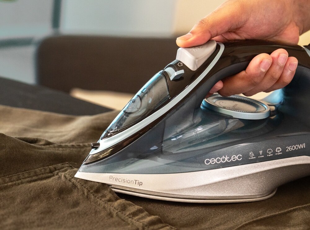 Osoba trzyma żelazko z napisem \'cectec 2600W\' i \'PrecisionTip\', prasując materiał. Żelazko ma przezroczysty zbiornik na wodę i pokrętło do regulacji temperatury.