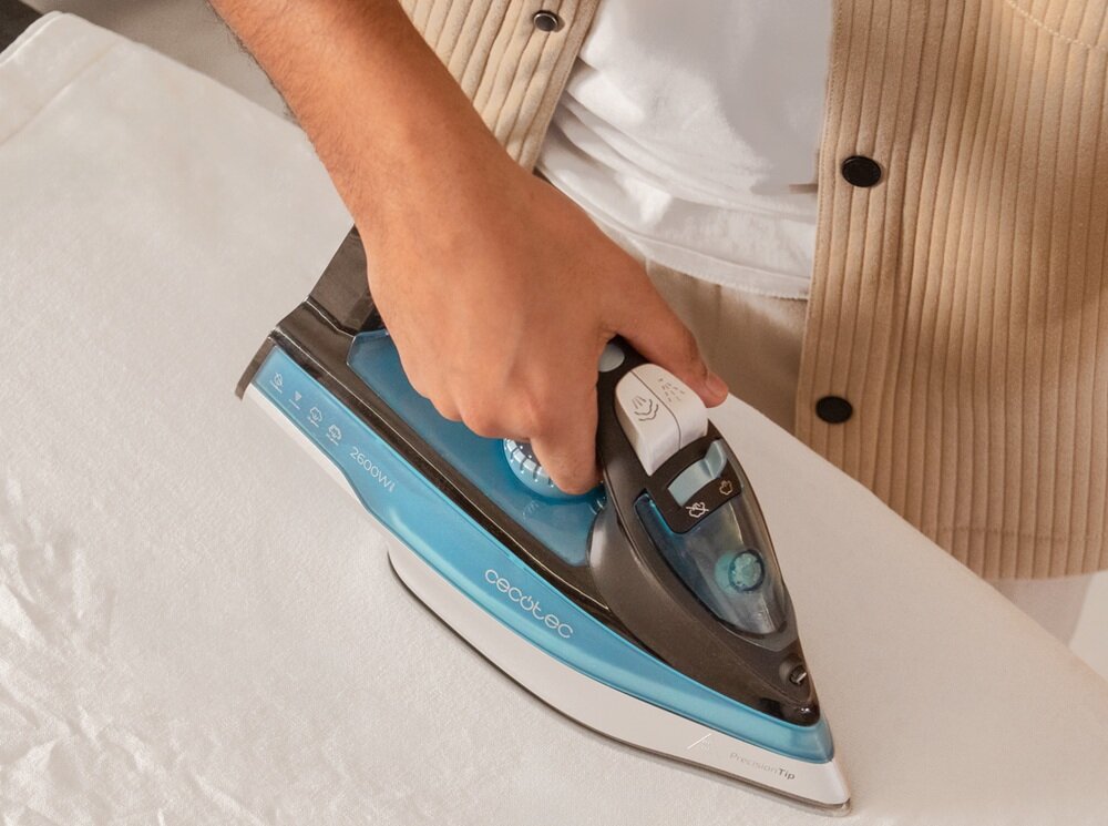 Osoba prasuje białą tkaninę żelazkiem marki Cecotec, model IronHero 2600W. Na żelazku widoczne są napisy \'cecotec\' i \'2600W\'.