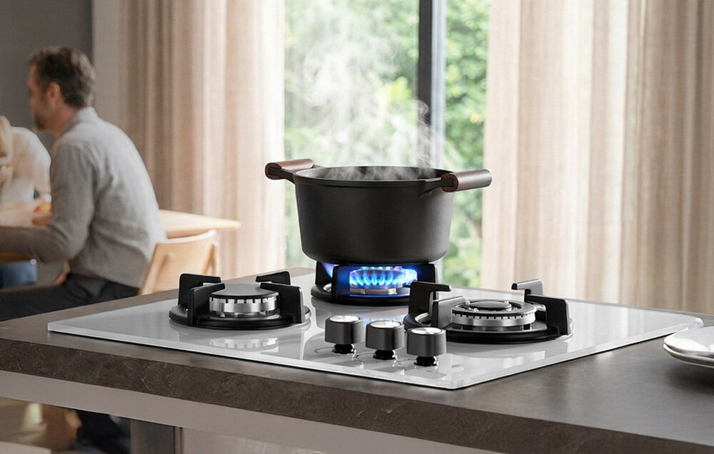 Płyta gazowa ISEASY MGBG-603 Garnek stoi na środkowym palniku płyty gazowej, na którym widać intensywny, równy płomień. Tło z jadalnią dodaje scenie domowego, ciepłego charakteru płyta gazowa trójpalnikowa 3 strefy gotowania szkło 3,3kW 2,7kW 1,75kW