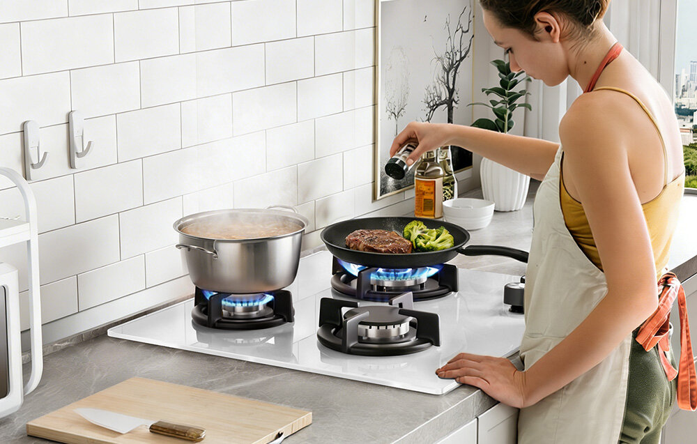 Płyta gazowa ISEASY MGBG-603 Osoba przygotowuje posiłek na płycie gazowej z 3 palnikami, gotując w dużym garnku oraz smażąc mięso z warzywami na patelni. Przyprawia potrawę, dodając składniki bezpośrednio podczas gotowania, a cała scena ukazuje wygodną i dobrze zorganizowaną przestrzeń kuchenną 3 palniki niezależne sterowanie równoczesne gotowanie organizacja
