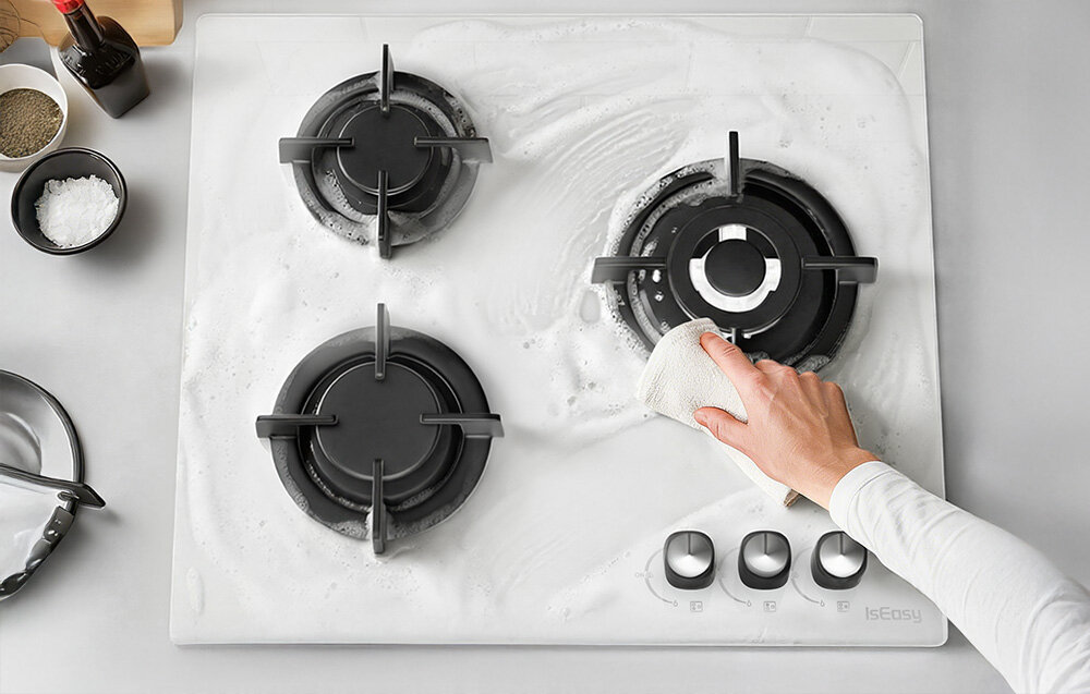 Płyta gazowa ISEASY MGBG-603 Na płycie rozprowadzono pianę czyszczącą, a dłoń wyciera powierzchnię miękką ściereczką. Pokazuje to łatwość utrzymania płyty w czystości, dzięki gładkiej strukturze szkło łatwe czyszczenie estetyka gładka powierzchnia