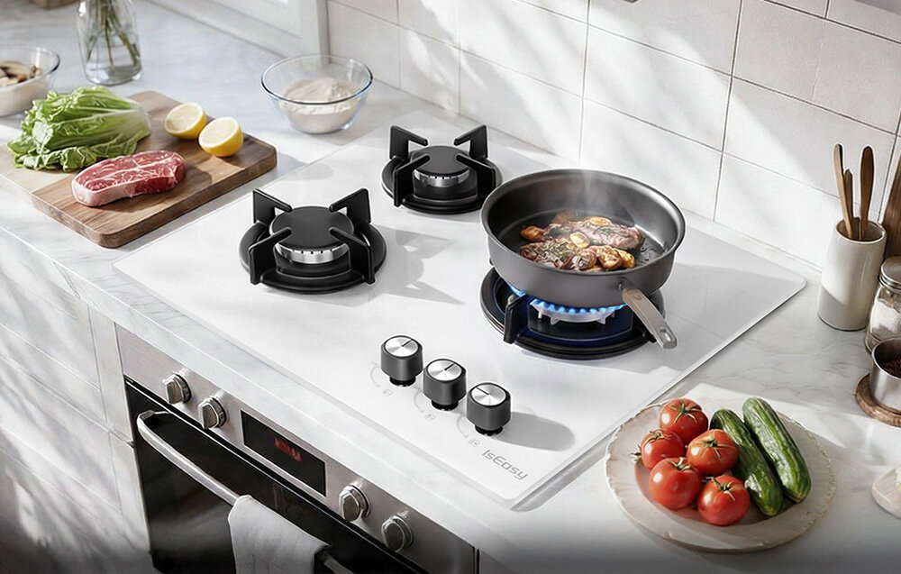 Płyta gazowa ISEASY MGBG-603 Na płycie gazowej stoi patelnia z podsmażanymi składnikami, a obok ułożono świeże produkty gotowe do gotowania. Kadr podkreśla funkcjonalność trzech palników i ich równomierny płomień montaż instalacja pokrętła zapłon regulacja